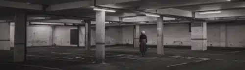 Lonely woman in a dark, empty parking garage – symbolic of fear, surveillance, and urban insecurity.