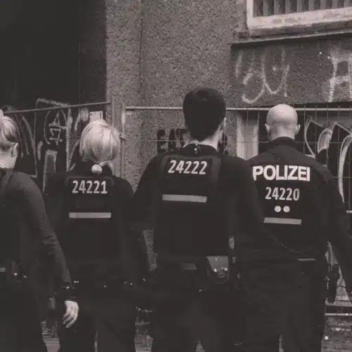 Polizisten stehen mit dem Rücken zur Kamera vor einer mit Graffiti bemalten Hauswand