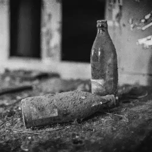 Leere Bierflaschen in einem verfallenen Raum als Symbol für Alkoholmissbrauch, soziale Ausgrenzung und familiäre Gewalt in Nil by Mouth (1997)