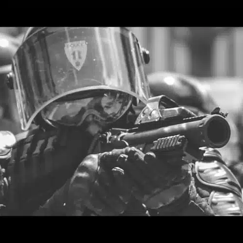Eine Gruppe von Polizisten, die nebeneinander stehen und Tränengas verschießen.