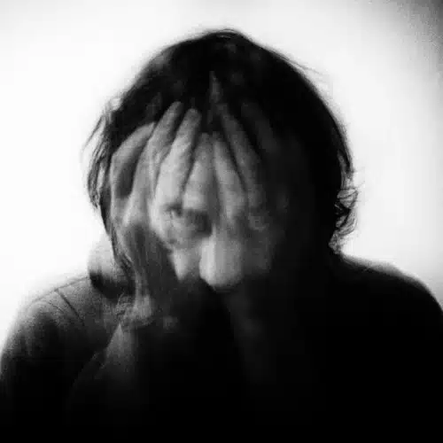 Verzweifelte Person mit vor das Gesicht geschlagenen Händen als Symbol für Angst, Abschreckung und Jugenddelinquenz.