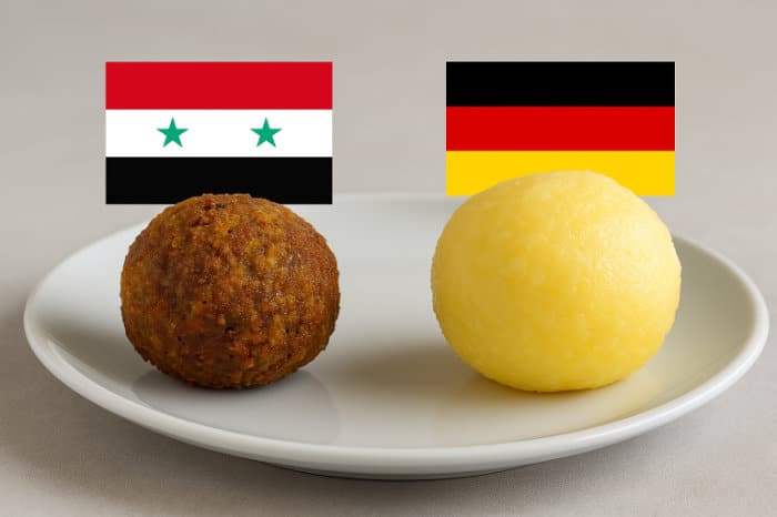Ein Falafel neben einem Kartoffelkloß vor einer syrischen bzw. deutschen Flagge
